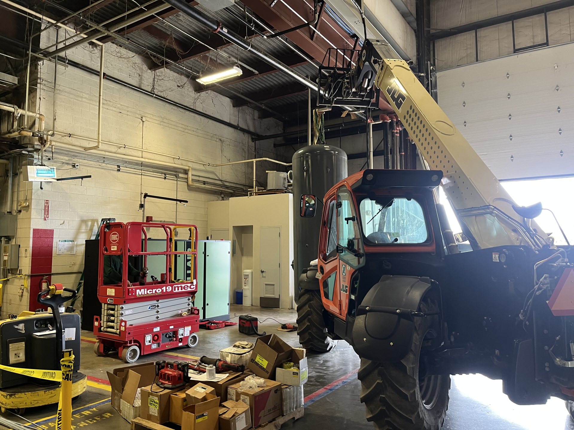Telehandler and scissor lift rigging a large air receiver tank in a mechanical room in Virginia